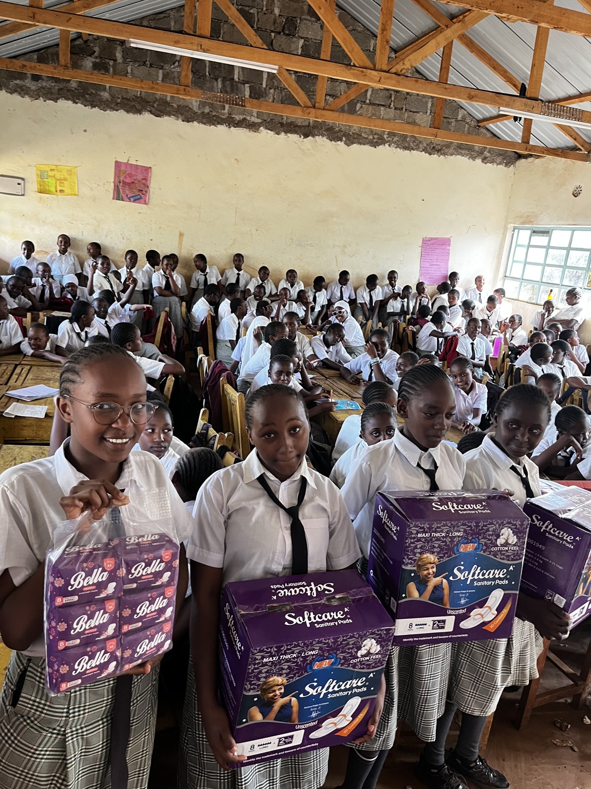 Students gathered at a school outreach event holding boxes of sanitary pads